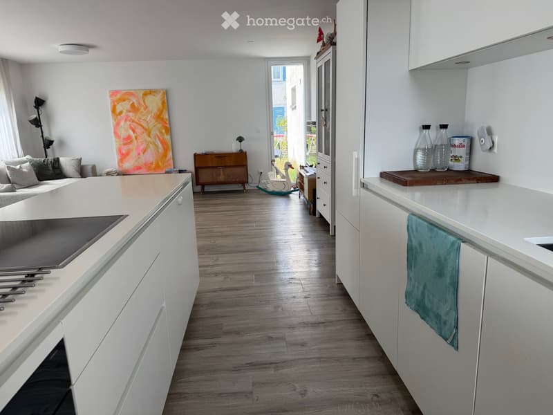 Open-plan living and kitchen area with white cabinets, wooden flooring, a sofa, and a kitchen island.