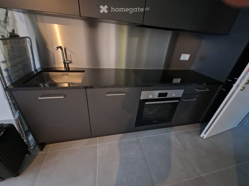 Modern kitchen with stainless steel sink, faucet, built-in oven, and dark grey cabinets.