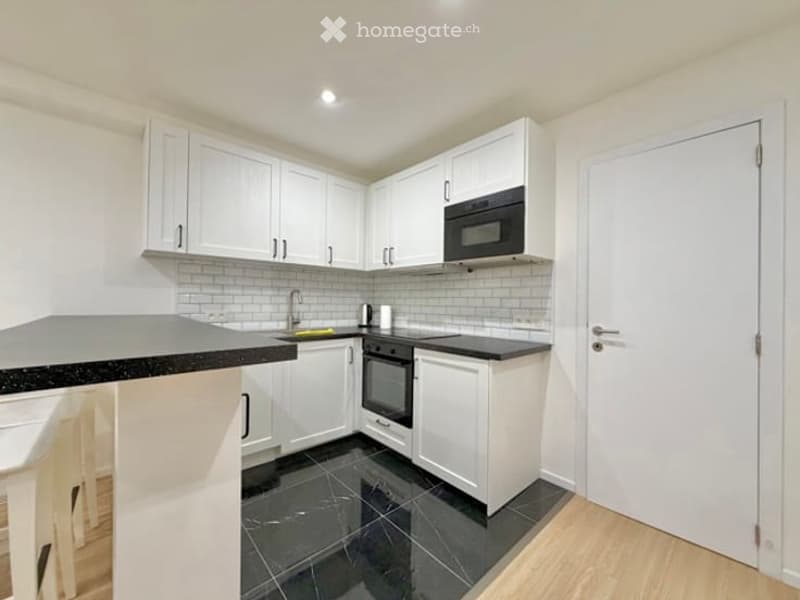 Modern kitchen with white cabinets, black countertops, and a black tiled floor. Features a microwave, oven, and sink.