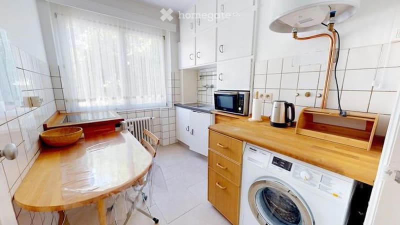 Bright kitchen with white cabinets, wooden countertops, and a small dining area. Includes a microwave, kettle, and a washing machine.