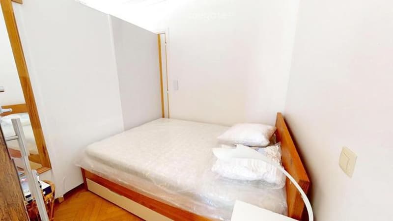 Small bedroom with a single bed, white pillows, wooden headboard, and light wooden flooring.