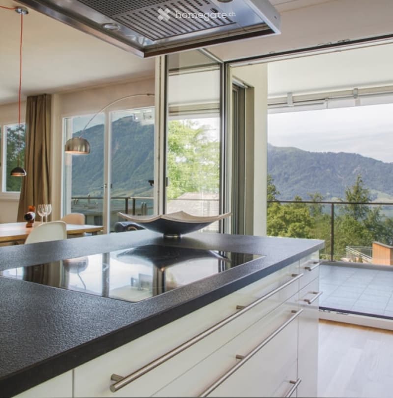 Modern kitchen with white cabinets, black countertop, large windows offering a scenic mountain view, and a sleek bowl on the counter.