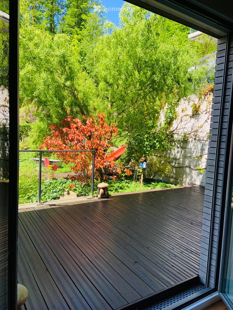 Wooden deck with metal railing, surrounded by lush greenery and trees, with a small birdhouse and a stone lantern visible.