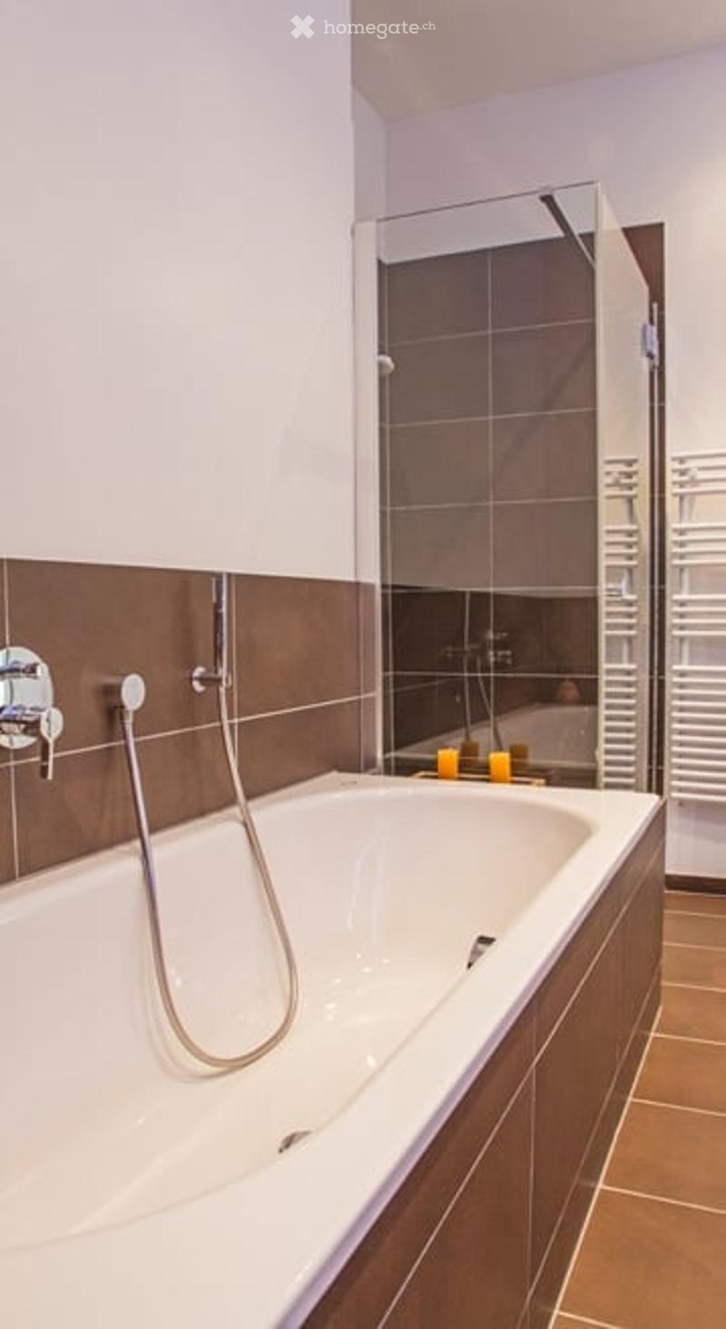 Modern bathroom with a white bathtub, chrome faucet, glass-enclosed shower, and brown tiled walls.