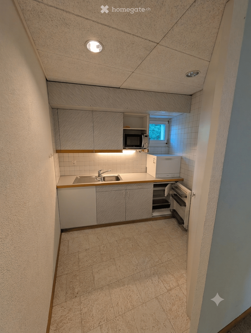 Compact kitchen with white cabinets, a sink, microwave, and refrigerator. The space features tiled walls and a tiled floor.