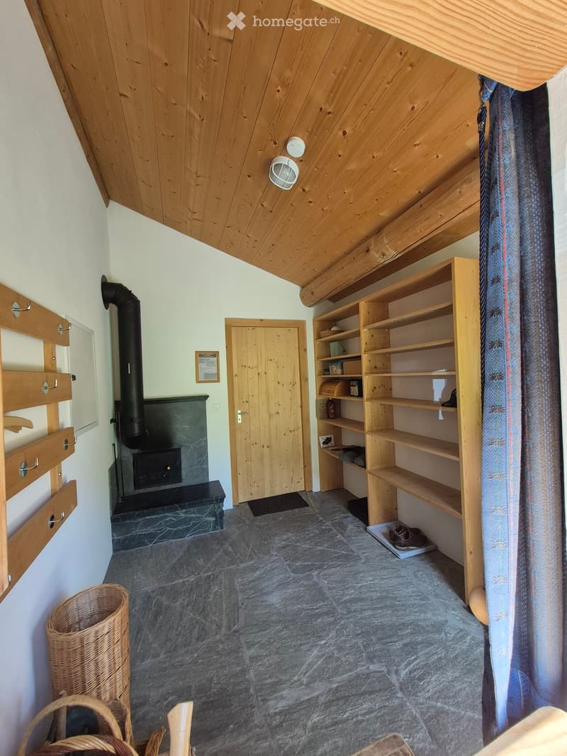 Cozy hallway with wooden beams, stone floor, built-in wooden shelves, fireplace, and a small entryway leading to another room.