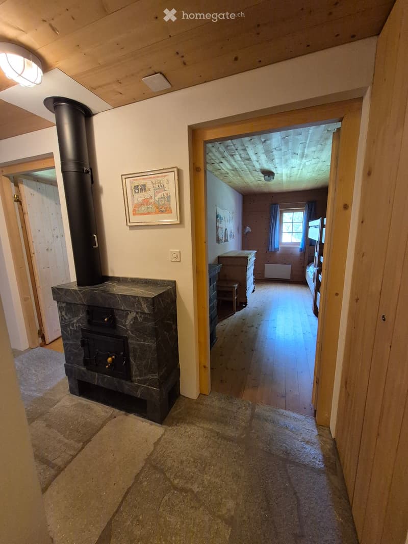 A wooden-floored hallway with a stone fireplace and a view into a bedroom with wooden furniture and a window.