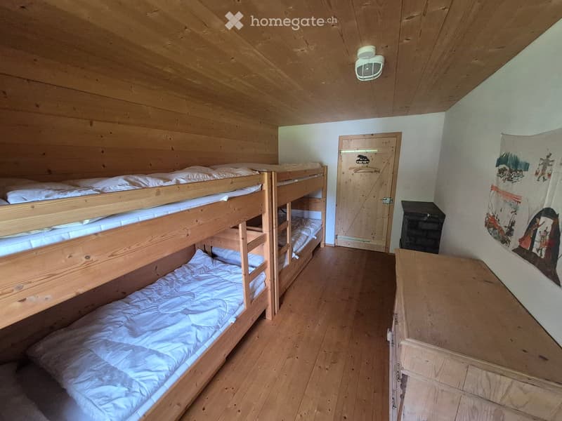 Cozy wooden bedroom with bunk beds, a small table, and a wardrobe. The room features wooden walls and a slanted wooden ceiling.