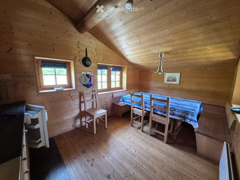 Cozy wooden room with slanted ceiling, wooden floor, table with chairs, small fridge, and a frying pan hanging on the wall.