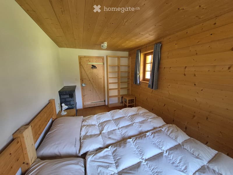 Cozy wooden bedroom with a large bed, nightstand, lamp, small stool, and a wooden shelf unit.