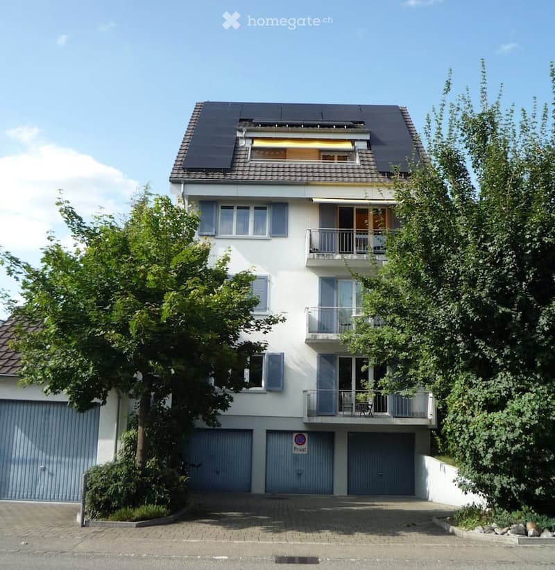 Two-story house with white exterior, multiple balconies, solar panels on the roof, and two garage doors.