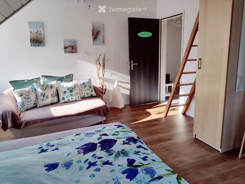 Bedroom with a bed, couch, wooden floor, white walls, and a door.