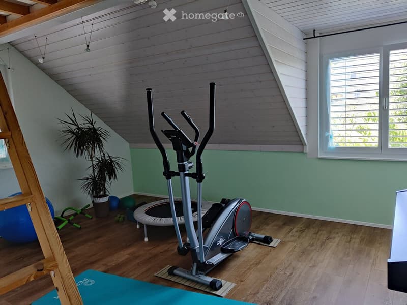 Well-lit room with wooden flooring, elliptical trainer, exercise ball, yoga mat, potted plant, foam roller, and treadmill.