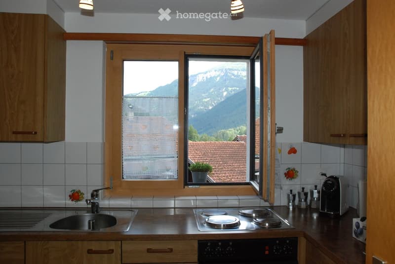 A modern kitchen with wooden cabinets, stainless steel appliances, and a scenic mountain view through large windows.