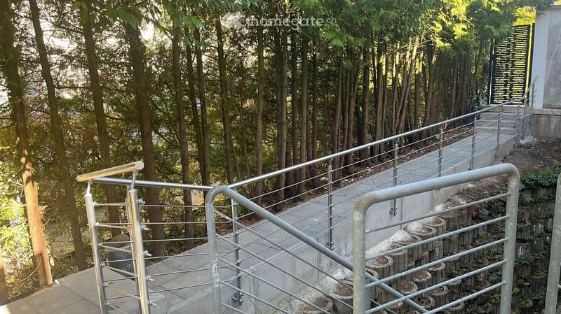 A raised ground floor pathway with metal railings, surrounded by trees and greenery.