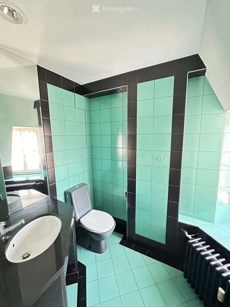 Modern bathroom with mint green tiles, black accents, a white toilet, a sink with a modern faucet, and a large mirror above the sink.