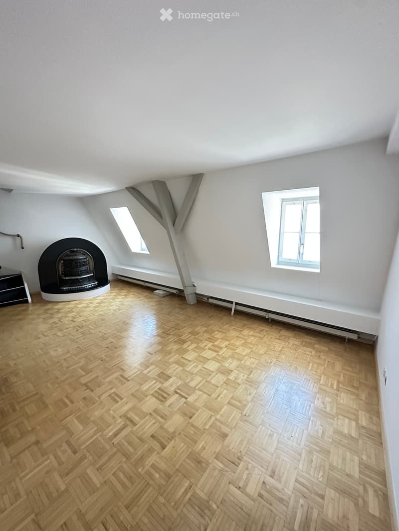 Room with wooden herringbone flooring, white walls, and a fireplace. Two windows provide natural light.