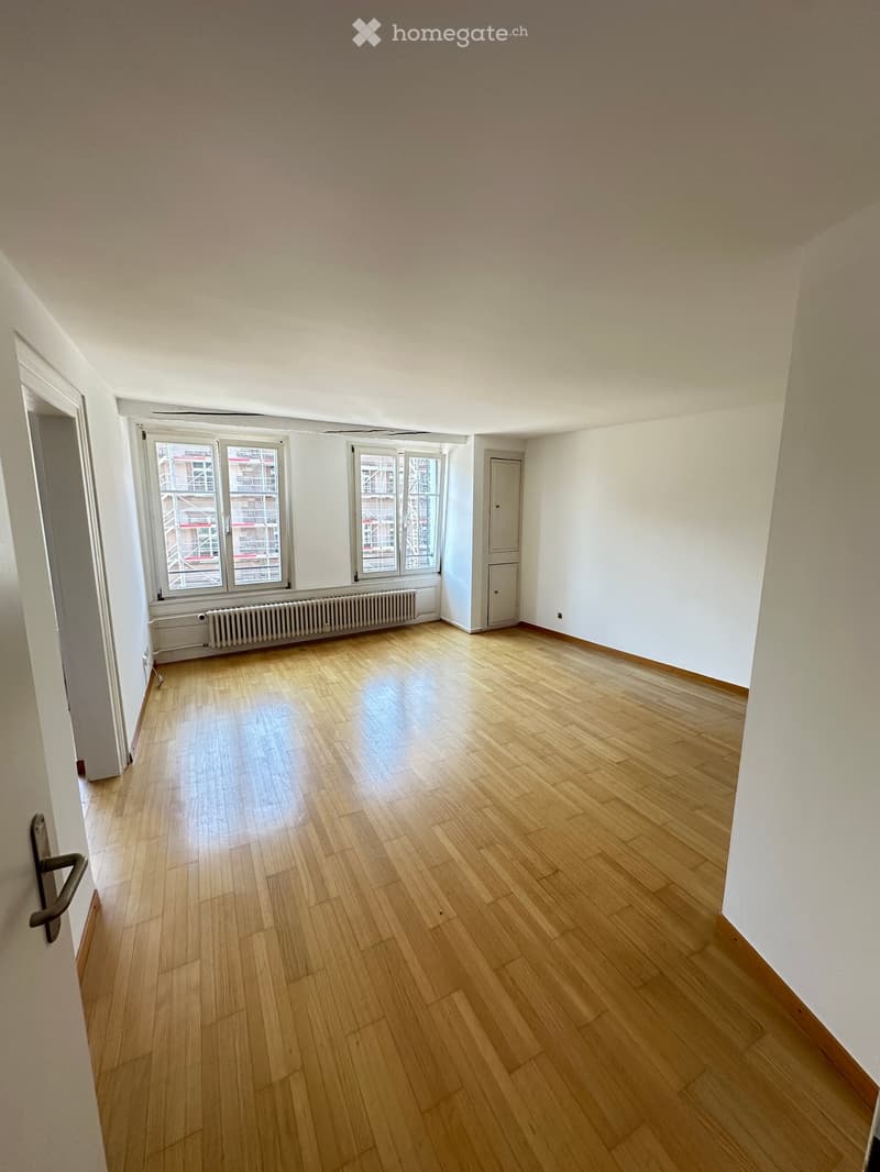 Empty room with wooden flooring, white walls, large windows, and a radiator. No furniture or equipment present.