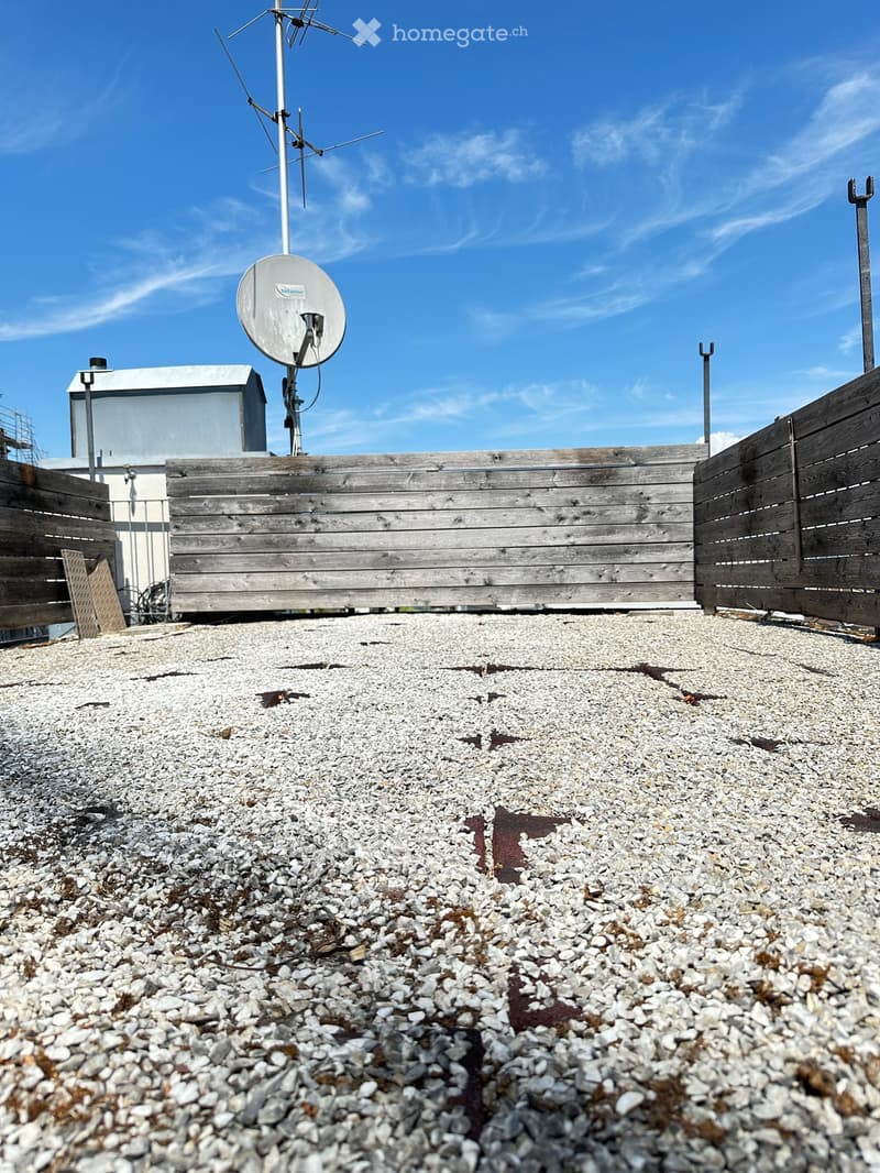 Roof terrace with gravel surface, wooden fencing, and a satellite dish mounted on a pole.
