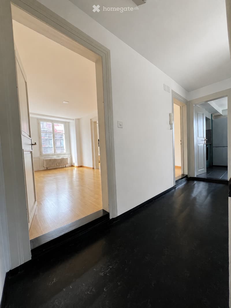 Empty hallway with white walls, black polished floor, wooden flooring in adjacent room, and visible doors leading to other spaces.