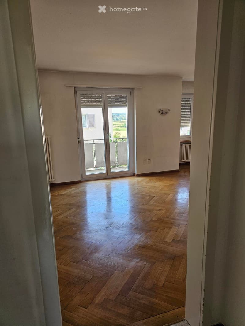 Empty room with wooden flooring, large sliding glass door leading to a balcony, and natural light coming in from the windows.