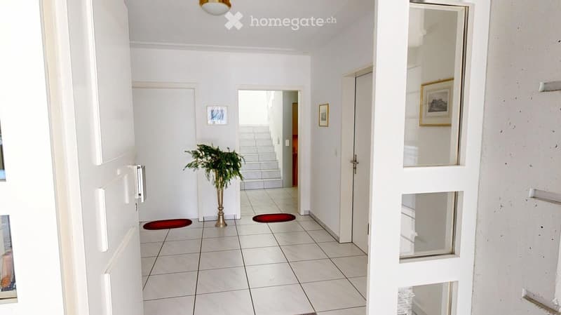 white tiled floor, white walls, red carpet, plant in a gold vase, white doors, picture frames, staircase