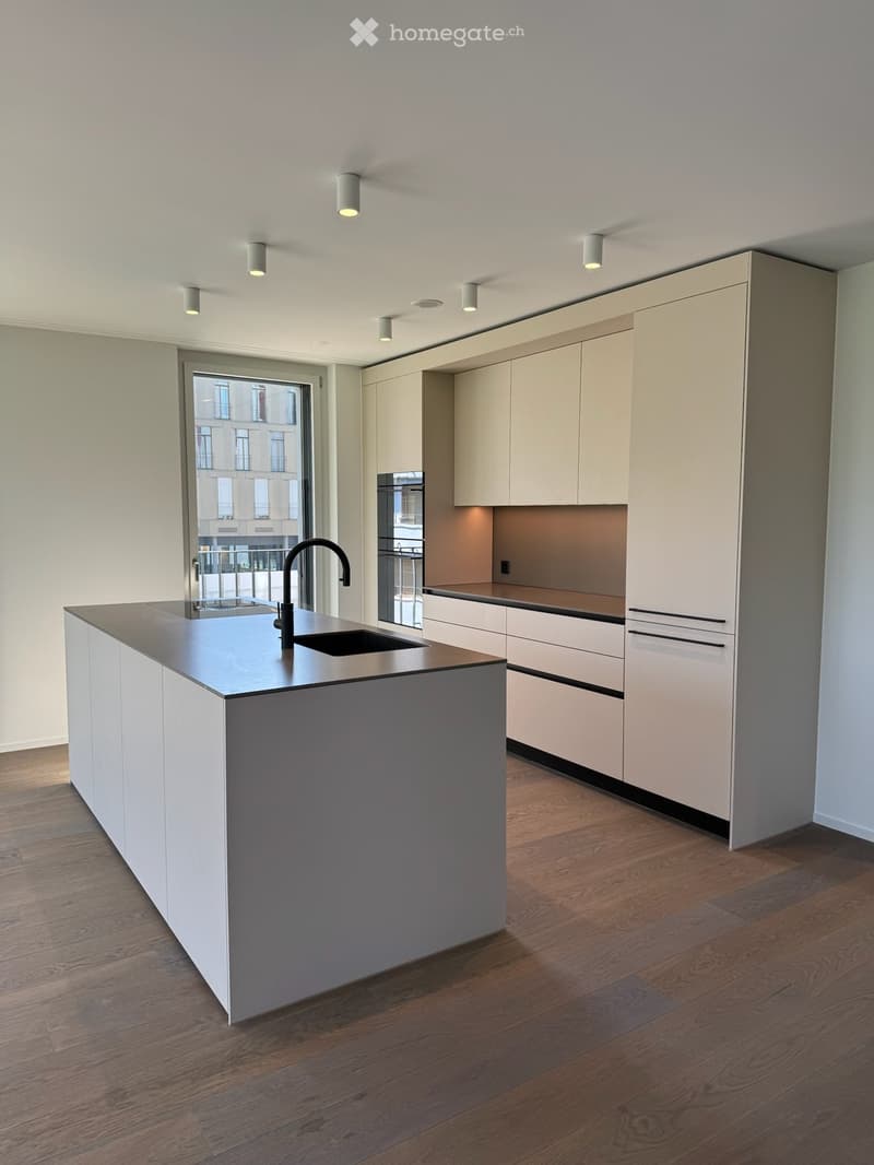Modern kitchen with white cabinetry, a central island, and a sink with a modern faucet. The space features wooden flooring and recessed lighting.