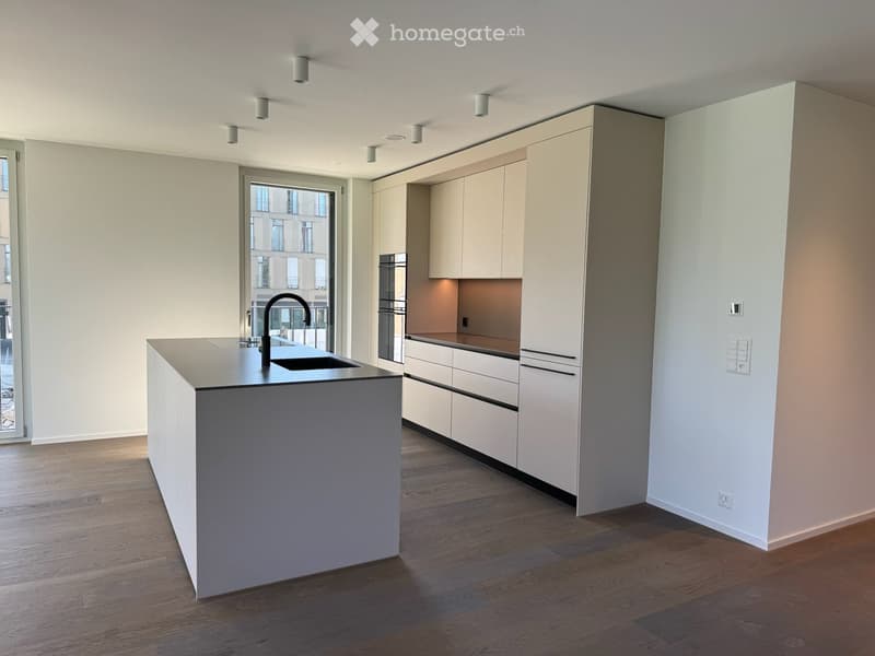 Modern kitchen with white cabinets, a central island, and a sink, featuring wooden flooring and recessed lighting.