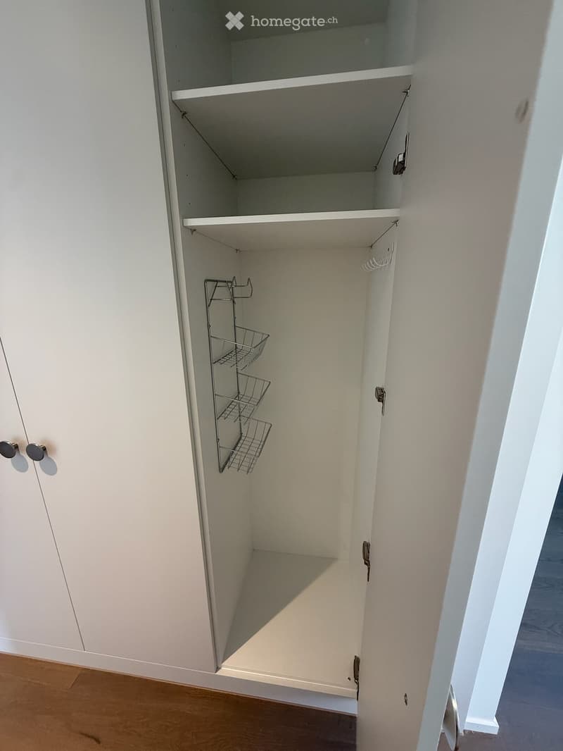 Empty white closet with two shelves and a wire basket on the lower shelf. The closet doors are open, revealing the interior space.