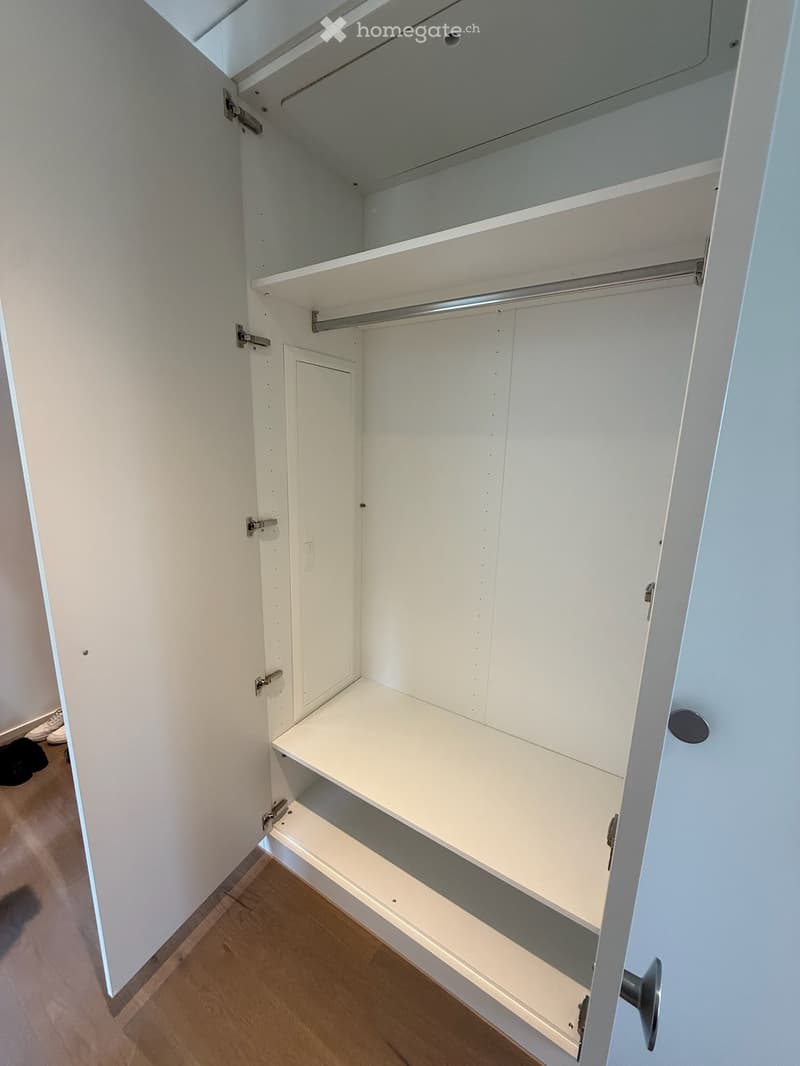 Empty closet with white walls, wooden floor, and multiple shelves and hanging rods.