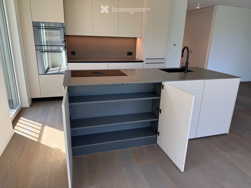 Modern kitchen with light-colored cabinets, a central island with an open shelf, a sink with a modern faucet, and an oven built into the cabinetry.