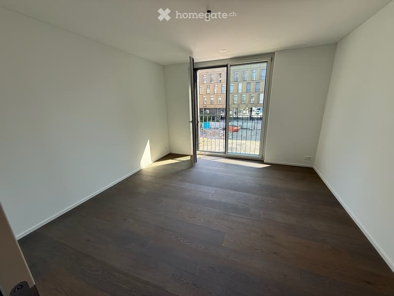 Empty room with wooden flooring, white walls, and a large sliding glass door leading to a balcony.