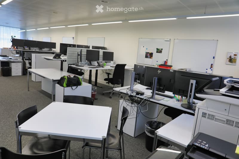 White cubicle desks, several monitors, chairs, whiteboards, trash cans, and printers.