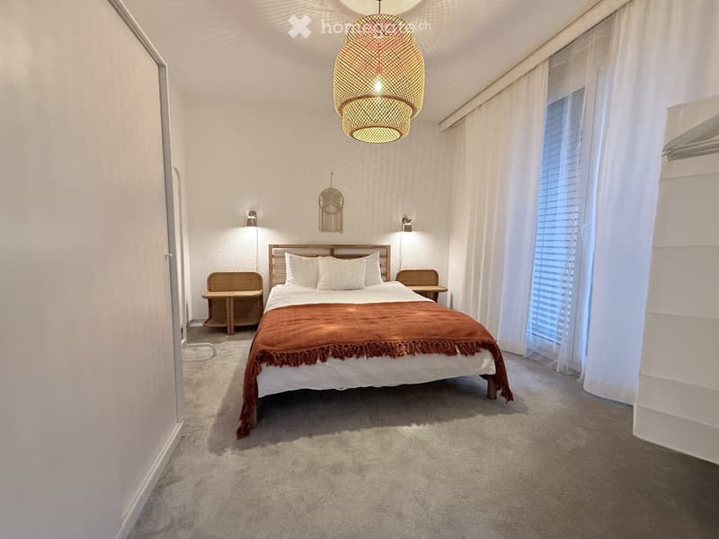 Cozy bedroom with a large bed, nightstands, a hanging pendant light, and a decorative wall piece.
