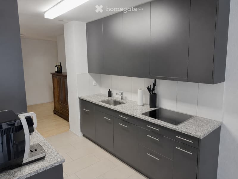 Modern kitchen with dark grey cabinets, granite countertops, stainless steel sink, coffee maker, and various small appliances.