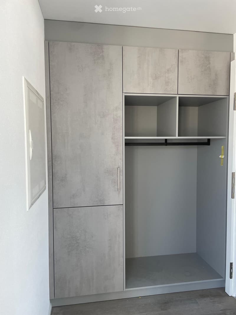 Empty closet with grey, textured cabinet doors and open shelving space. No furniture or items present.
