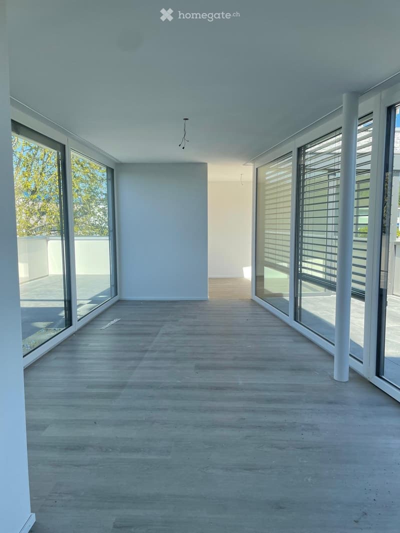 Empty room with light wooden flooring, large glass windows, and white walls. No furniture or equipment present.
