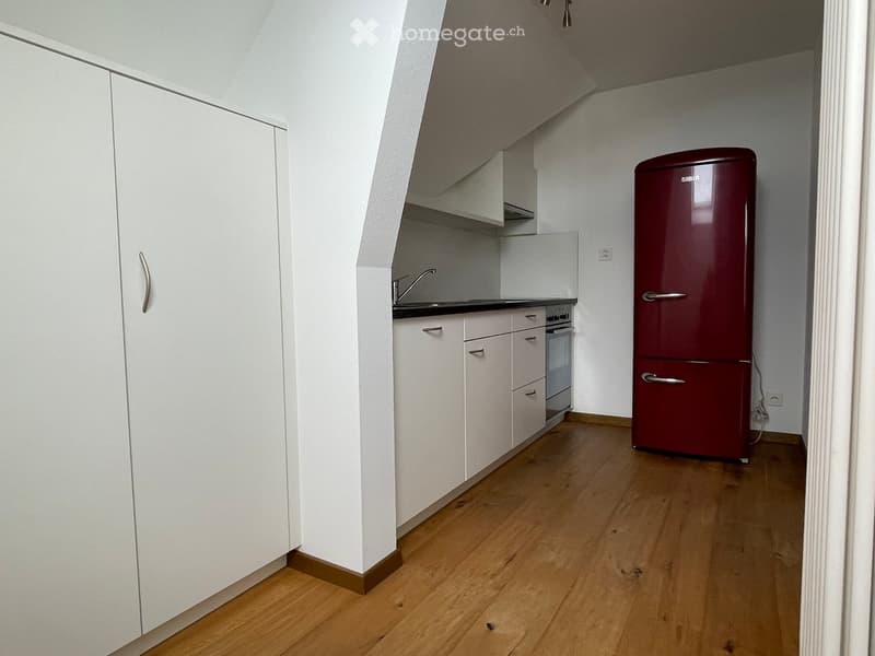 a room with kitchen and white walls, wooden floors, stainless steel appliances, white cabinets, sink and faucet, and a red refrigerator