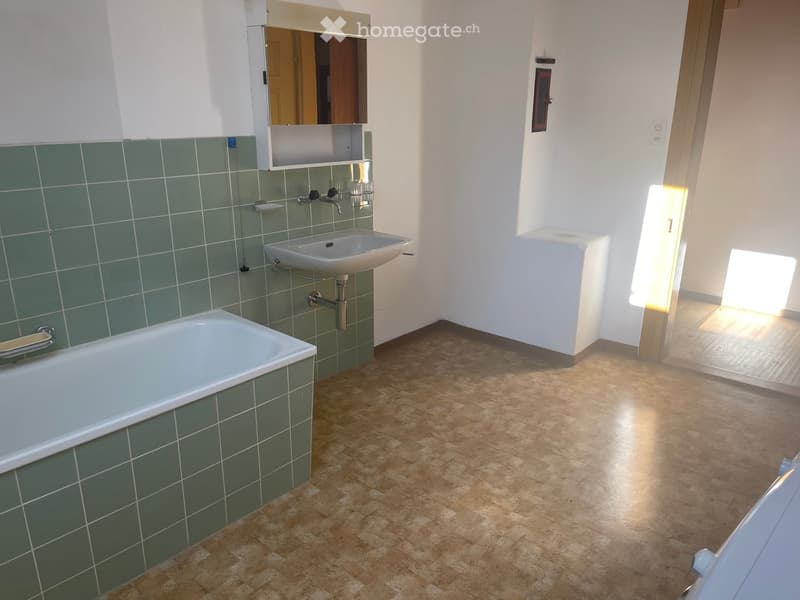 Bathroom with green tiles, white bathtub, sink, faucets, mirror above sink, small open door at far end