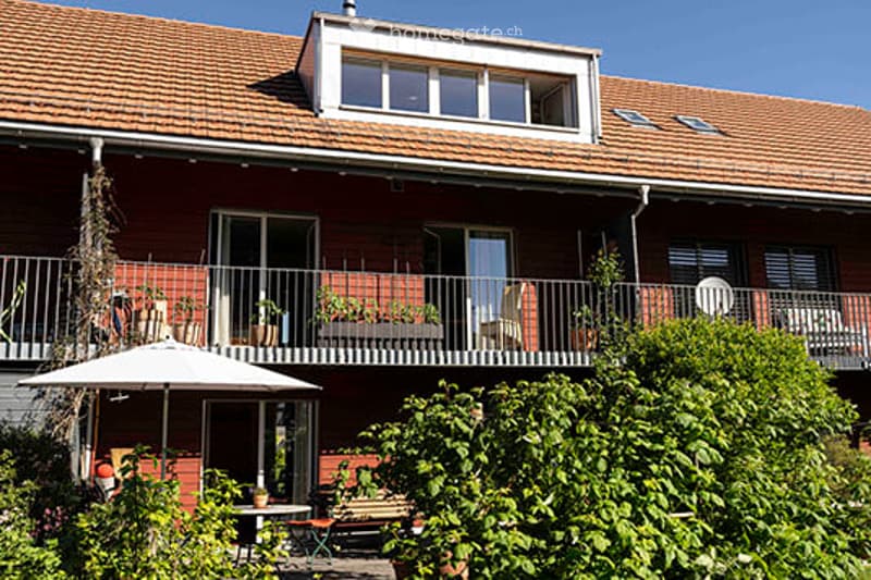 Red brick building with multiple balconies, large windows, and outdoor seating areas.