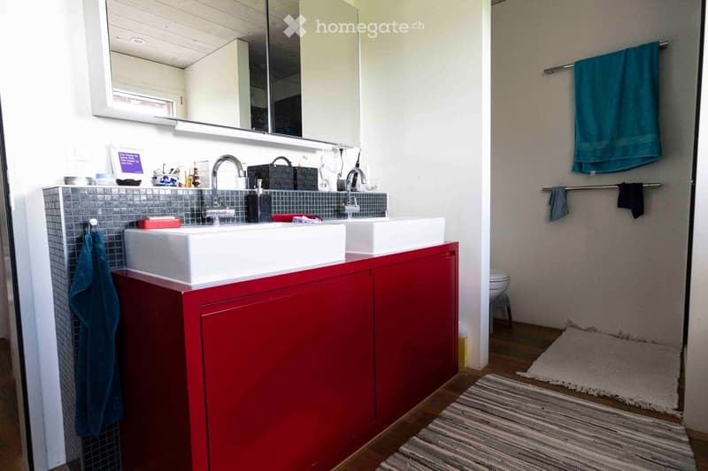 Modern bathroom with double sinks, red cabinet, large mirror, and towels hanging on racks.