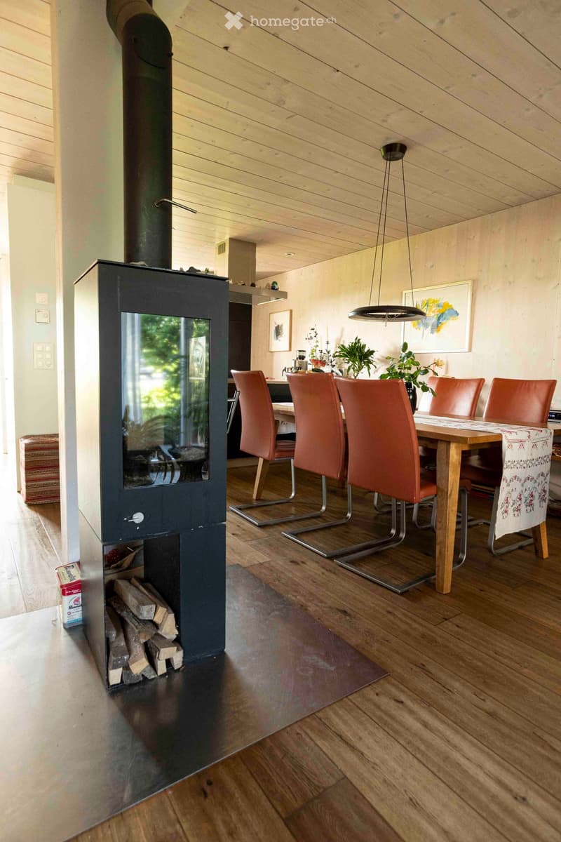Modern dining area with a wood-burning fireplace, wooden table, and orange chairs.
