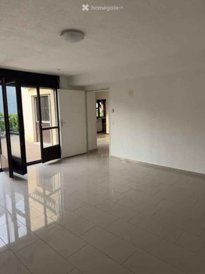 Empty room with tiled floor, white walls, and a large glass door leading to an outdoor area.