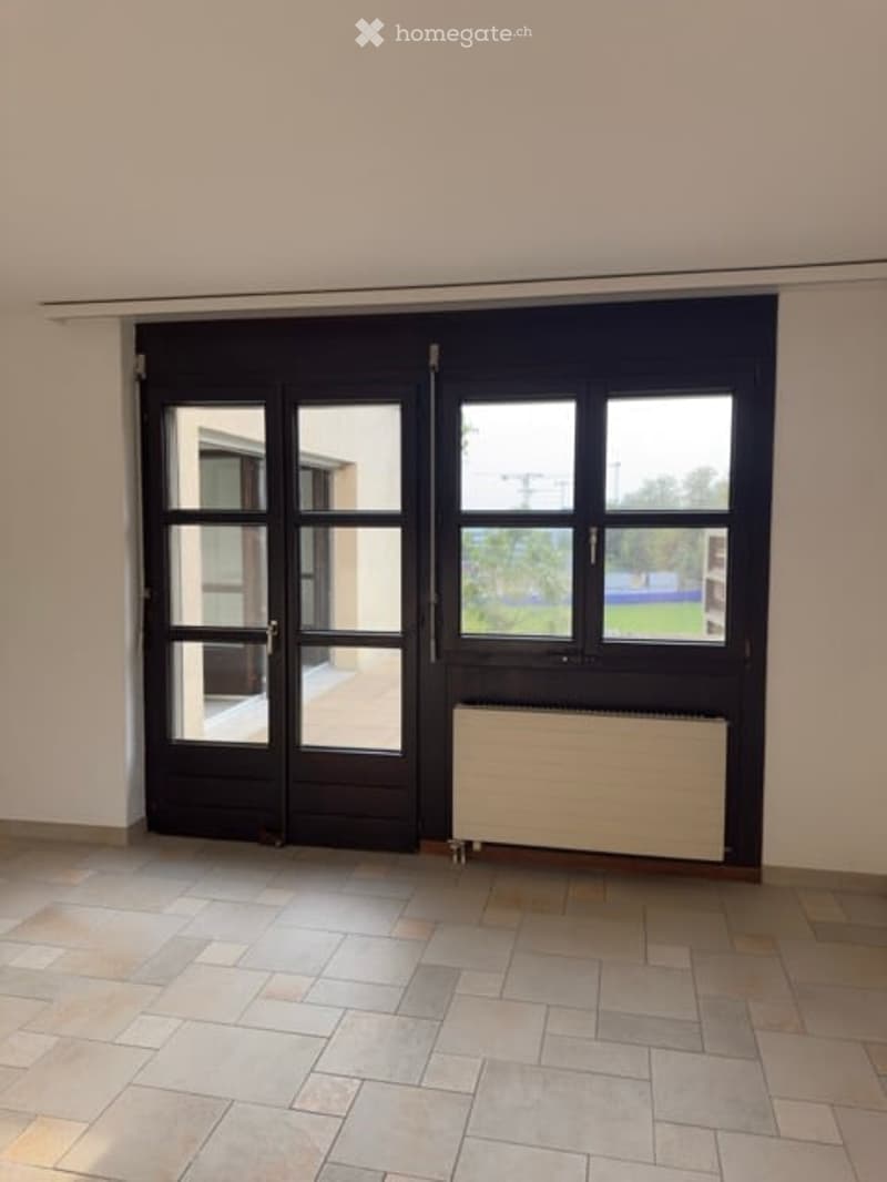 Empty room with tiled floor, white walls, large black double doors, and a radiator under the window.
