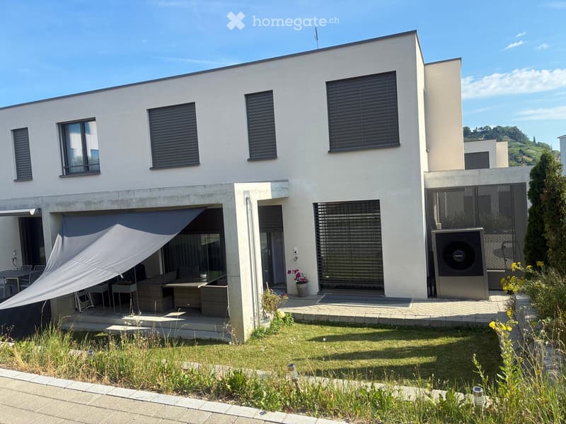 Modern two-story house with white facade, large windows, and a covered outdoor seating area with wicker furniture.