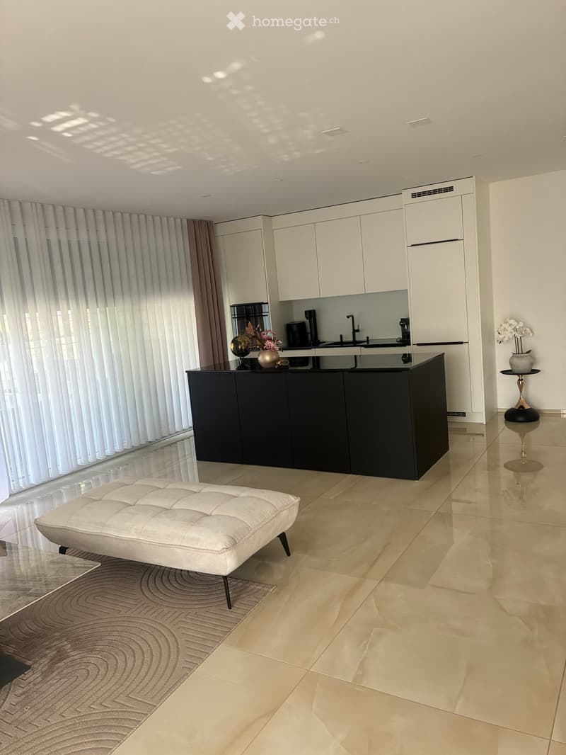 Modern kitchen and living area with white cabinets, black island, white sofa, and decorative items.