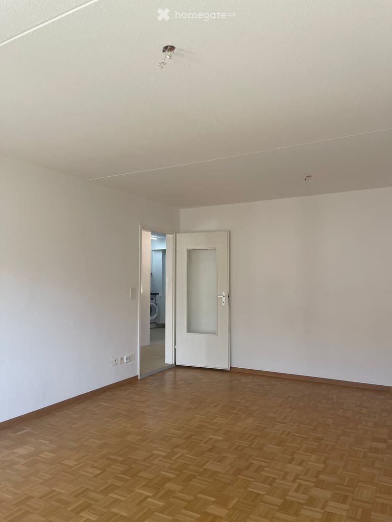 empty room with wooden floor, white walls, closed door and an open doorway to another room with a washing machine