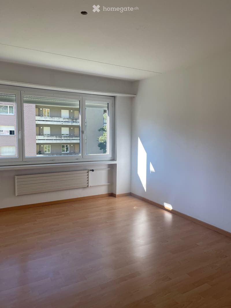 Empty room, white walls, wooden floor, large window with a view of the building