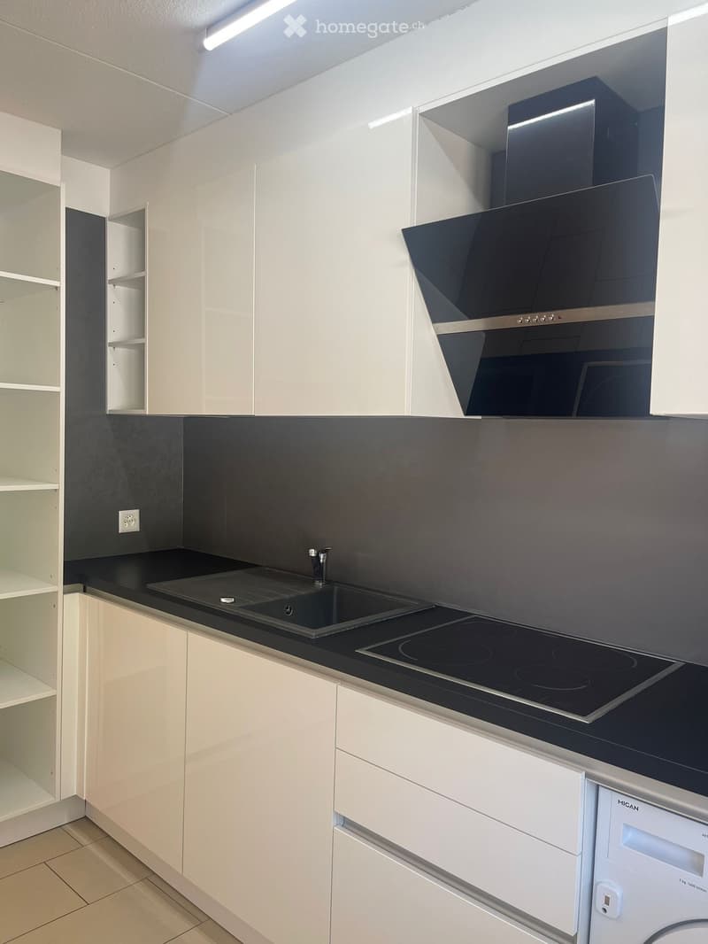 white cabinets, black countertops, built-in sink, modern stovetop, washing machine, exhaust hood