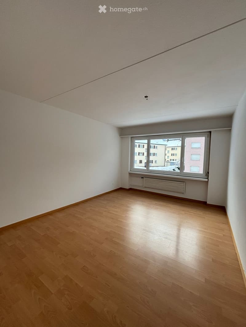 An empty room with wooden floor, white walls, large window, and white ceiling.